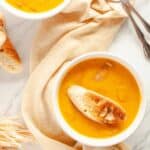 Two white bowls filled with Butternut Squash and Sausage Soup with toasted baguette