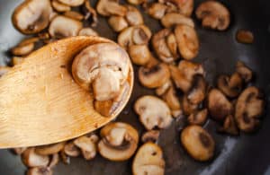 Wooden spoon over pan of sauteed mushrooms