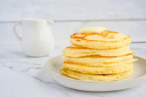 Stack of Mom's Buttermilk Pancakes on white plate and white syrup cup in background