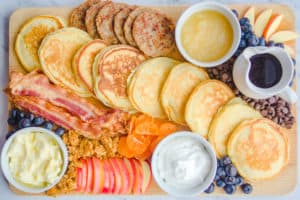 Wood cutting board with pancakes, toppings, bacon, sausage and fresh fruit 