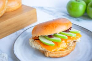 Granny apple chicken sandwich on a light gray plate with green apples and cutting board in background