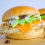 Two granny smith chicken sandwiches sitting on wood cutting board