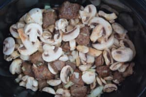 Browned meat, onions, mushrooms and beef consommé in the bottom of the slow cooker.