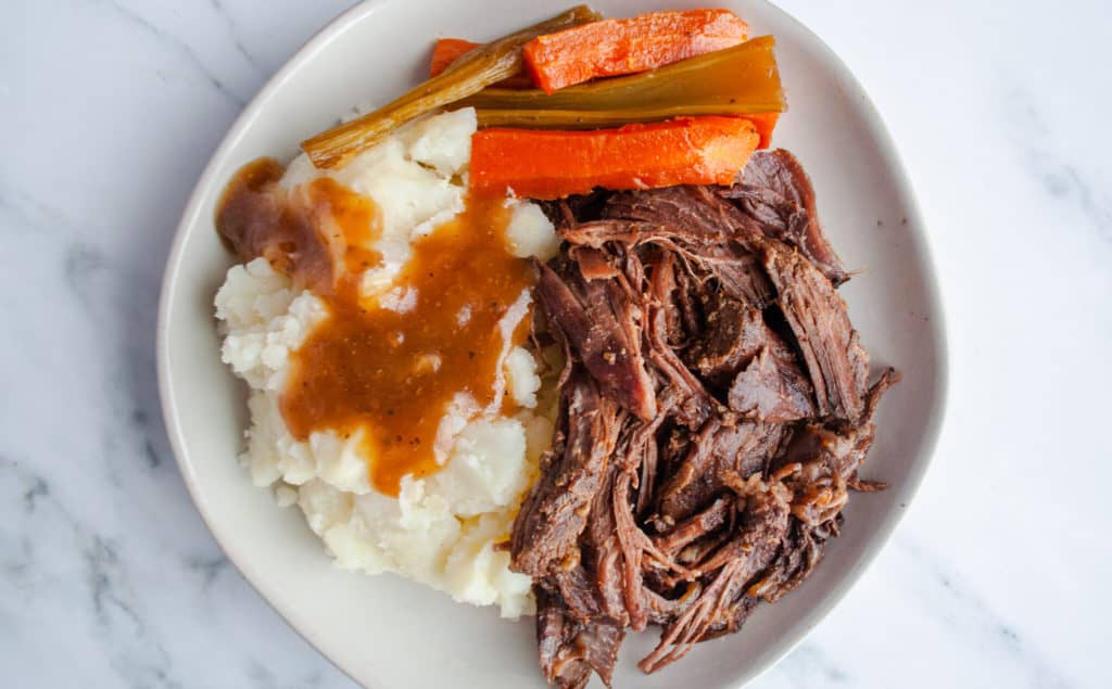 White plate of pot roast, carrots, celery, mashed potatoes and gravy