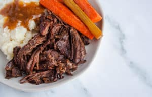 White plate of pot roast, carrots, celery, mashed potatoes and gravy
