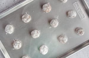 Molasses Cookie balls rolled in powdered sugar on a metal baking sheet.