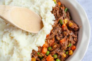 Wooden spoon spreading parmesan mashed potatoes over the Shepherd's Pie