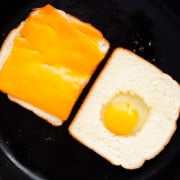 Slice of bread topped with cheddar and another with egg in a hole in cast iron skillet