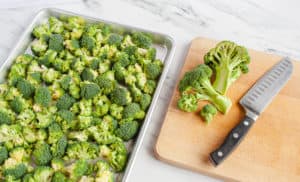 Raw broccoli florets on sheet pan and cut on a wooden cutting board