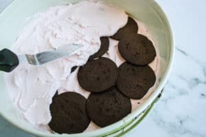 Metal spatula spreading raspberry whipped cream over wafer cookies