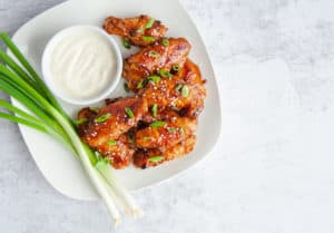 Honey Hoisin Chicken WIngs on white plate with side of ranch and green onion garnish