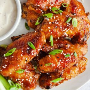 Honey Hoisin Chicken WIngs on white plate with side of ranch and green onion garnish