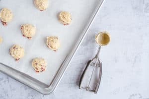 Scoops of cranberry cookie dough layed out on parchment covered baking sheet