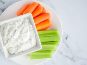White plate of baby carrots and celery slices with Skinny Ranch Dressing for dipping