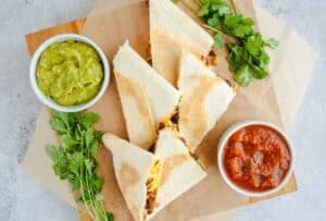 Mexican Breakfast Sheet Pan Quesadillas on wooden tray with guacamole, salsa and cilantro