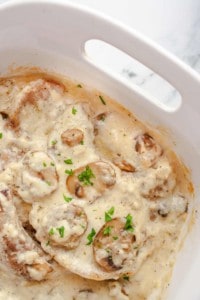 Pork Chops with Mushroom Gravy in white baking dish garnished with parsley