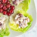 Grape Chicken Salad on butter lettuce leaves with a bunch of red grapes on a white plate