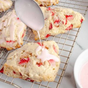 Metal spoon drizzling strawberry glaze over Strawberry Scones on a wire rack