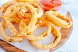 Beer Battered Onion Rings on wooden tray lined with parchment and a bowl of ketchup