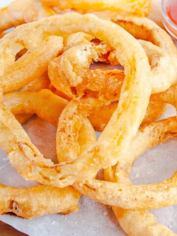 Beer Battered Onion rings on white parchment with bowl of ketchup in background