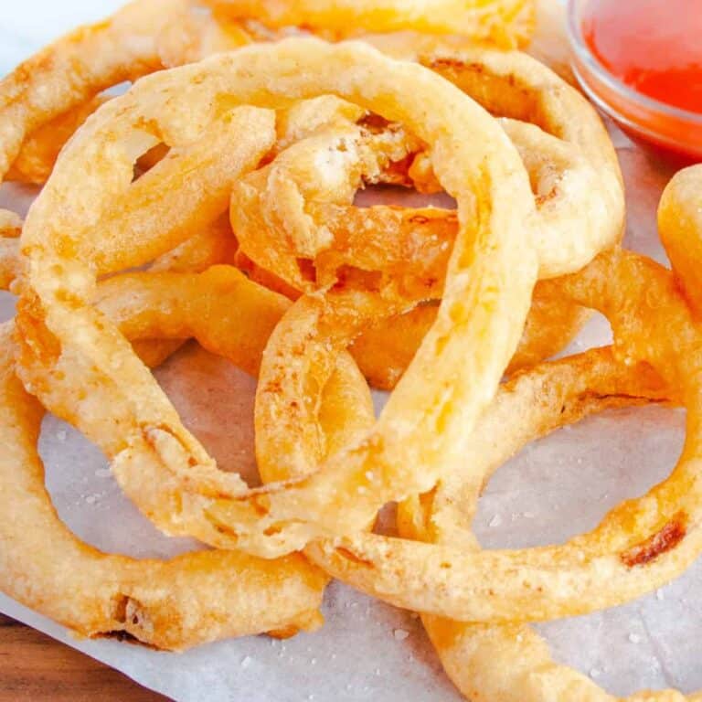 Beer Battered Onion rings on white parchment with bowl of ketchup in background