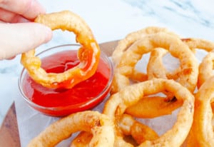 Onion ring being dipped in a bowl of ketchup