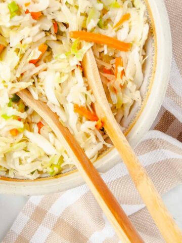 Two wooden spoons resting in bowl of Old Fashioned Coleslaw with Vinegar