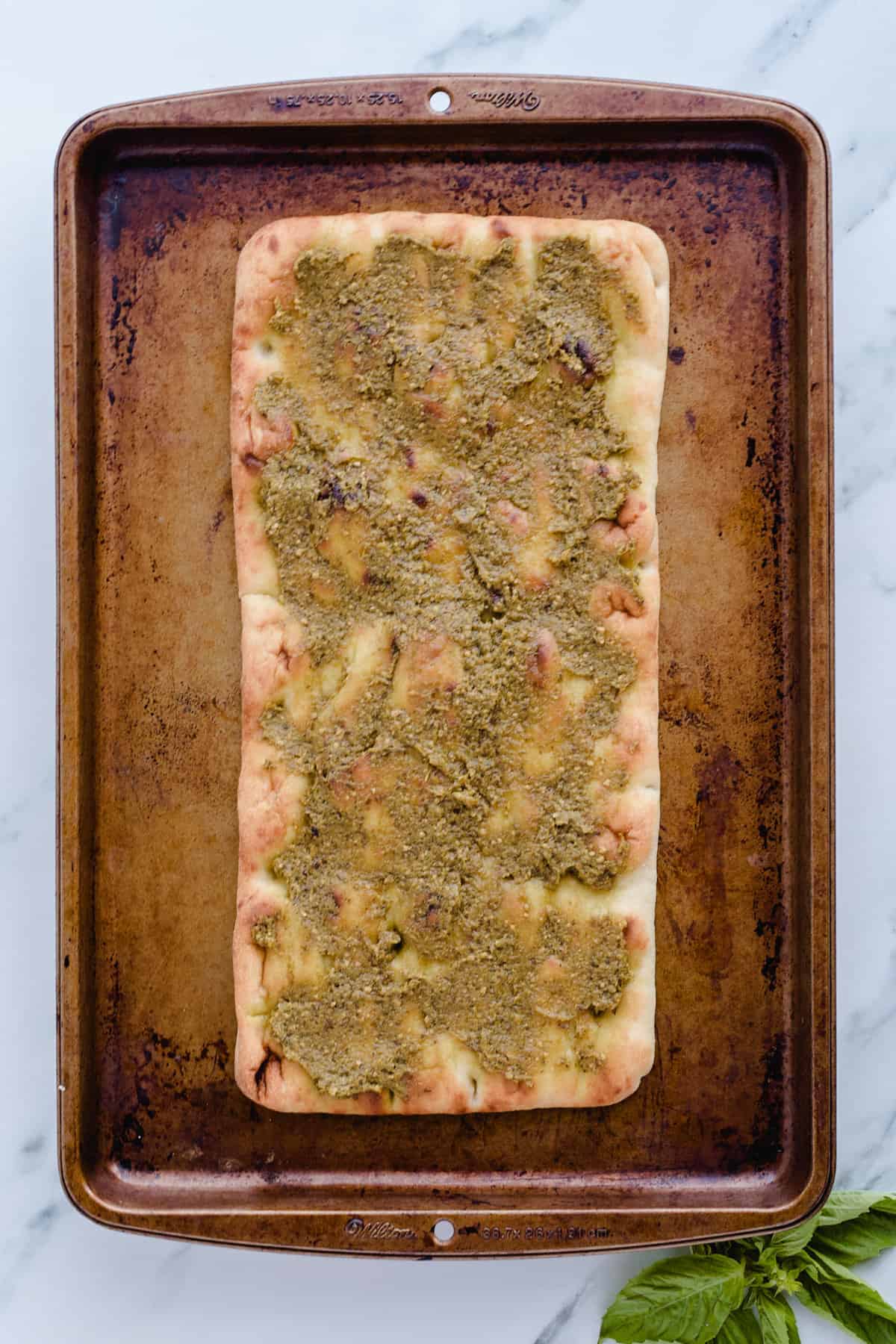 Pesto spread on top of flatbread on baking sheet