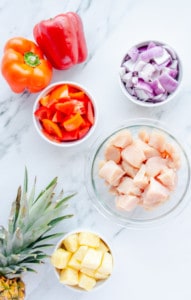 Bell peppers, red onion, chicken breast and pineapple on a marble countertop