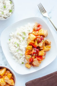 Hawaiian Chicken with Coconut Rice on a white plate with a gold fork and bowls of chicken and rice