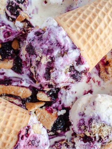 Two waffle cones filled with no-churn blueberry cheesecake ice cream laying in the loaf pan