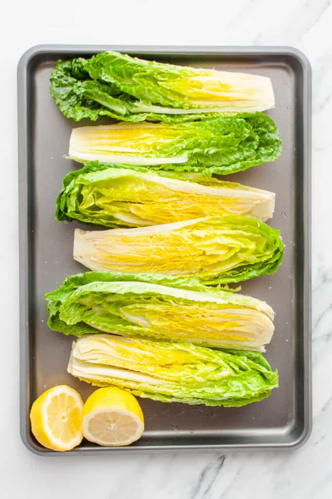 Raw romaine hearts on a sheet pan with a halved lemon