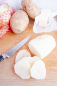 Slicing a peeled russet potato on a wooden cutting board