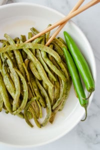 Sweet and Spicy Green Beans in a white bowl with chopsticks and whole green serrano peppers
