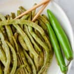 Sweet and Spicy Green Beans in a white bowl with chopsticks and whole green serrano peppers