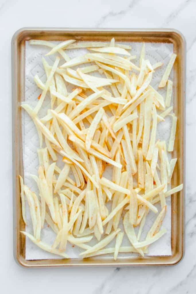 French fries after first fry laid out of a paper towel lined sheet pan