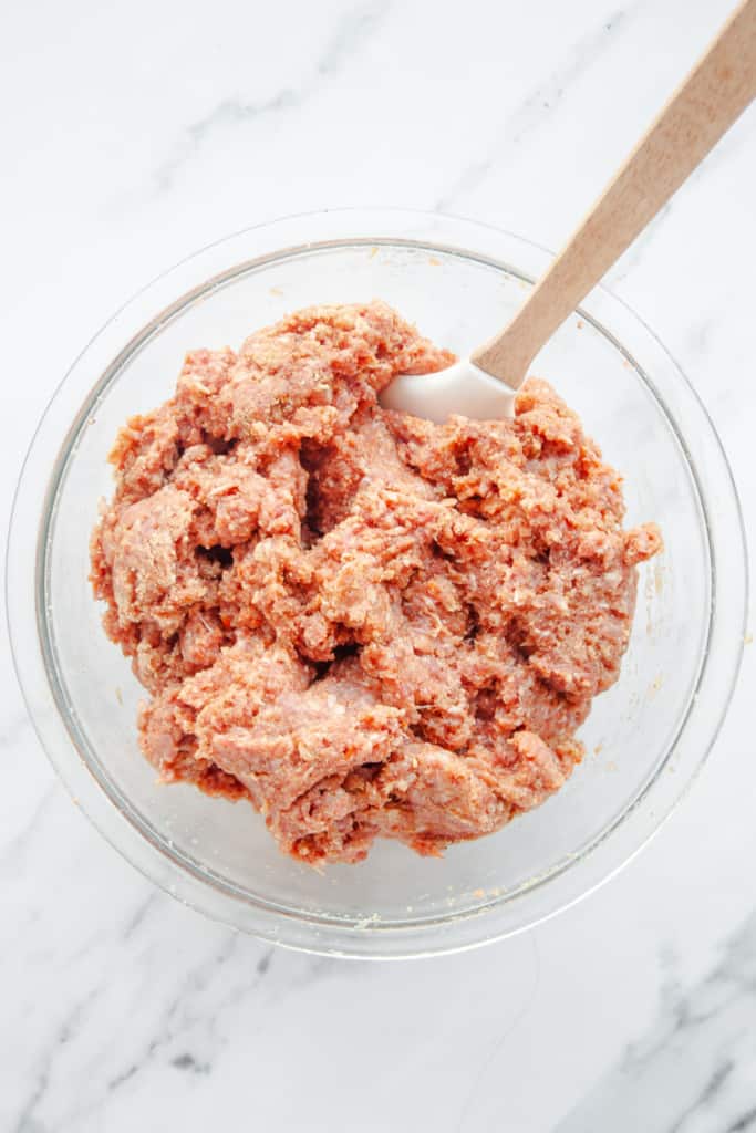 Raw meatball mixture in a glass bowl with spatula