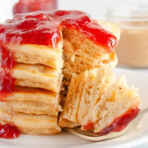 Fork holding pieces of peanut butter and jelly pancakes taken out of a stack