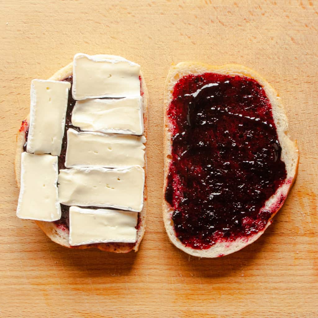 Blueberry jam and brie cheese spread out on two sourdough bread slices