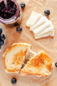 Brie Grilled Cheese on parchment paper with wedges of brie, blueberries and jam