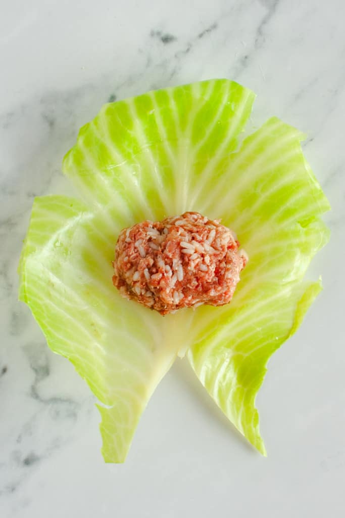 Cabbage leaf spread out on counter with mound of meat filling 