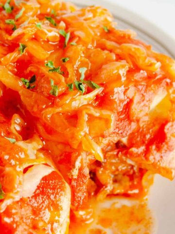 Two cabbage rolls on a plate with sauerkraut and tomato sauce