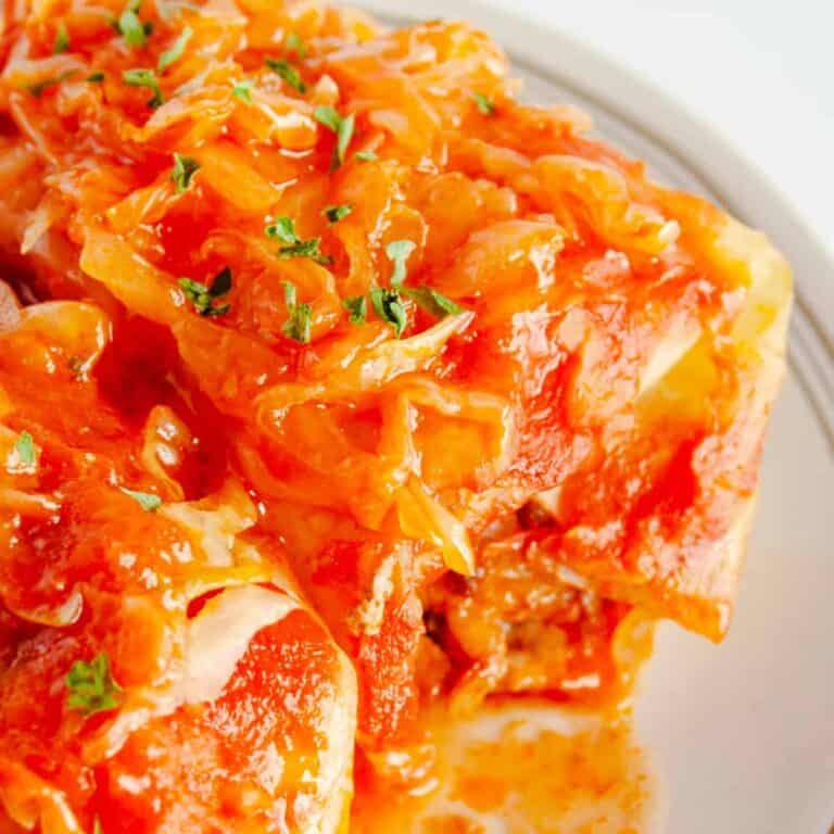 Two cabbage rolls on a plate with sauerkraut and tomato sauce
