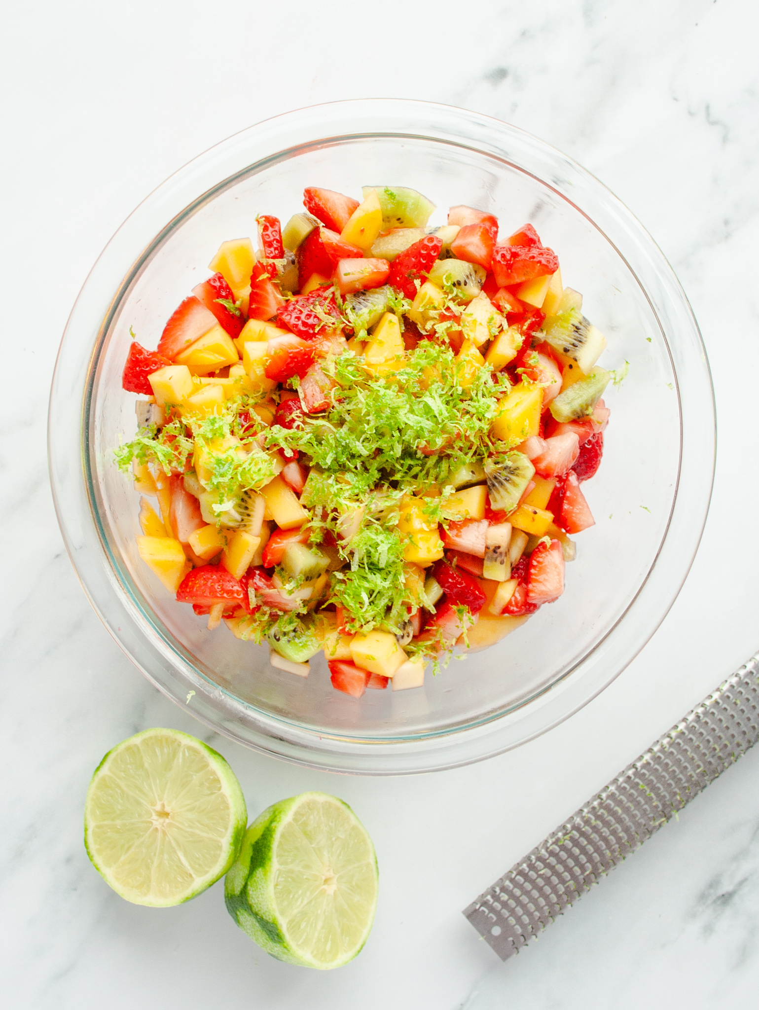 Lime zest grated on top of fruit in bowl.