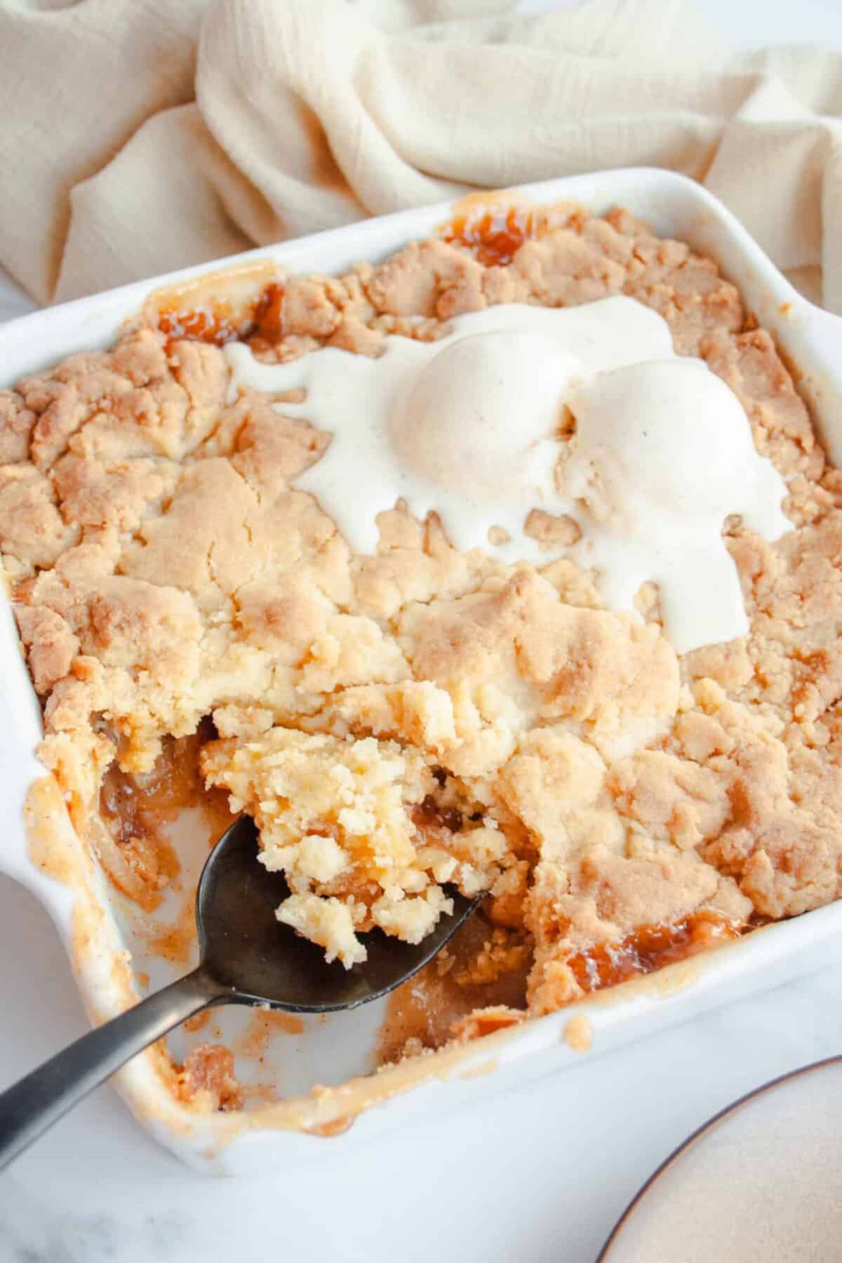 White pan of Cake Mix Apple Cobbler with a black serving spoon