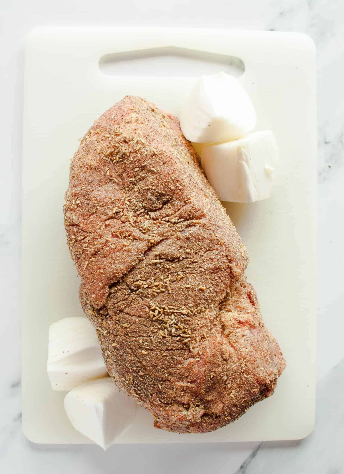 Seasoned pork roast on cutting board with quartered onion