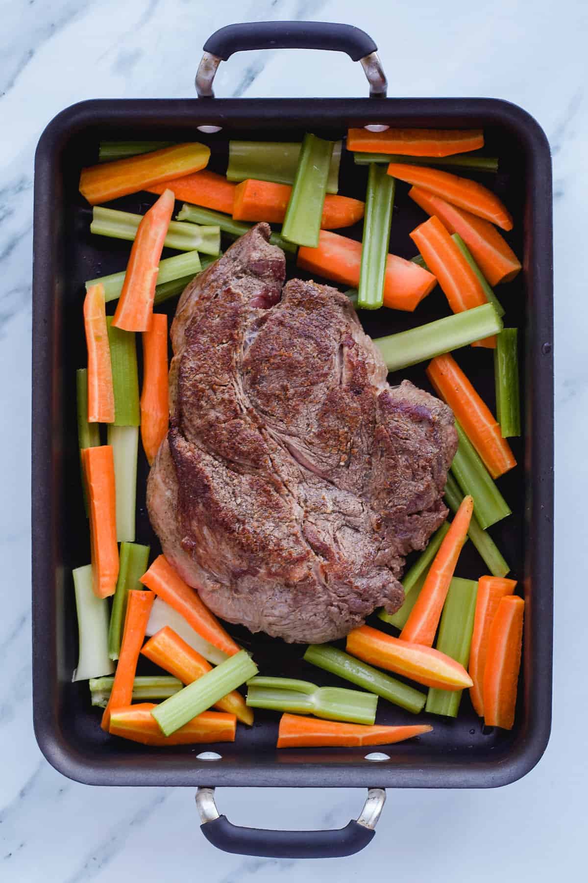 Seared chuck roast in pan with carrots and celery