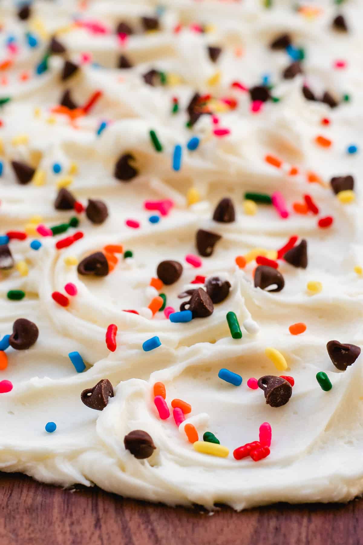 Close up of buttercream frosting on board with chocolate chips and rainbow sprinkles