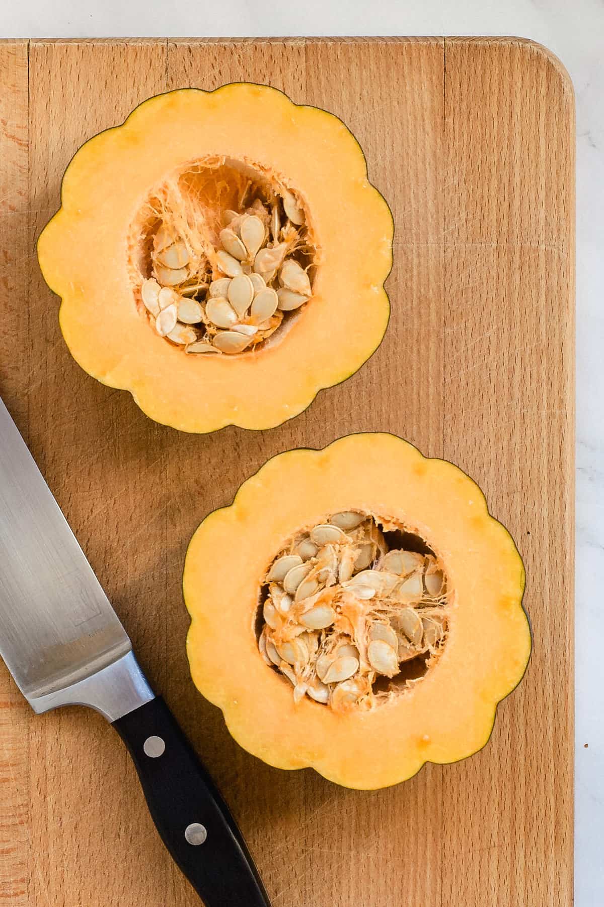 Acorn squash halves on a wooden cutting board with knife