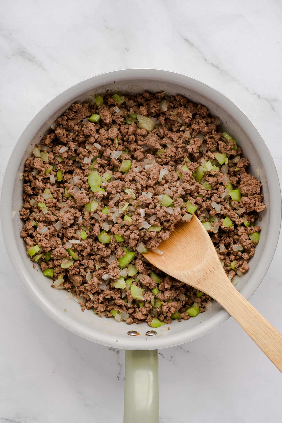 Ground beef, celery and onion cooked in skillet with wooden spoon
